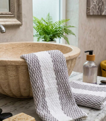 Nautica Home cotton bathing towel in white and grey stripe honeycomb texture draped over a marble bathroom sink in a luxury bathroom